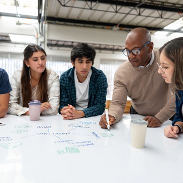 African American teacher giving tutoring a group of students at a community college - education concepts